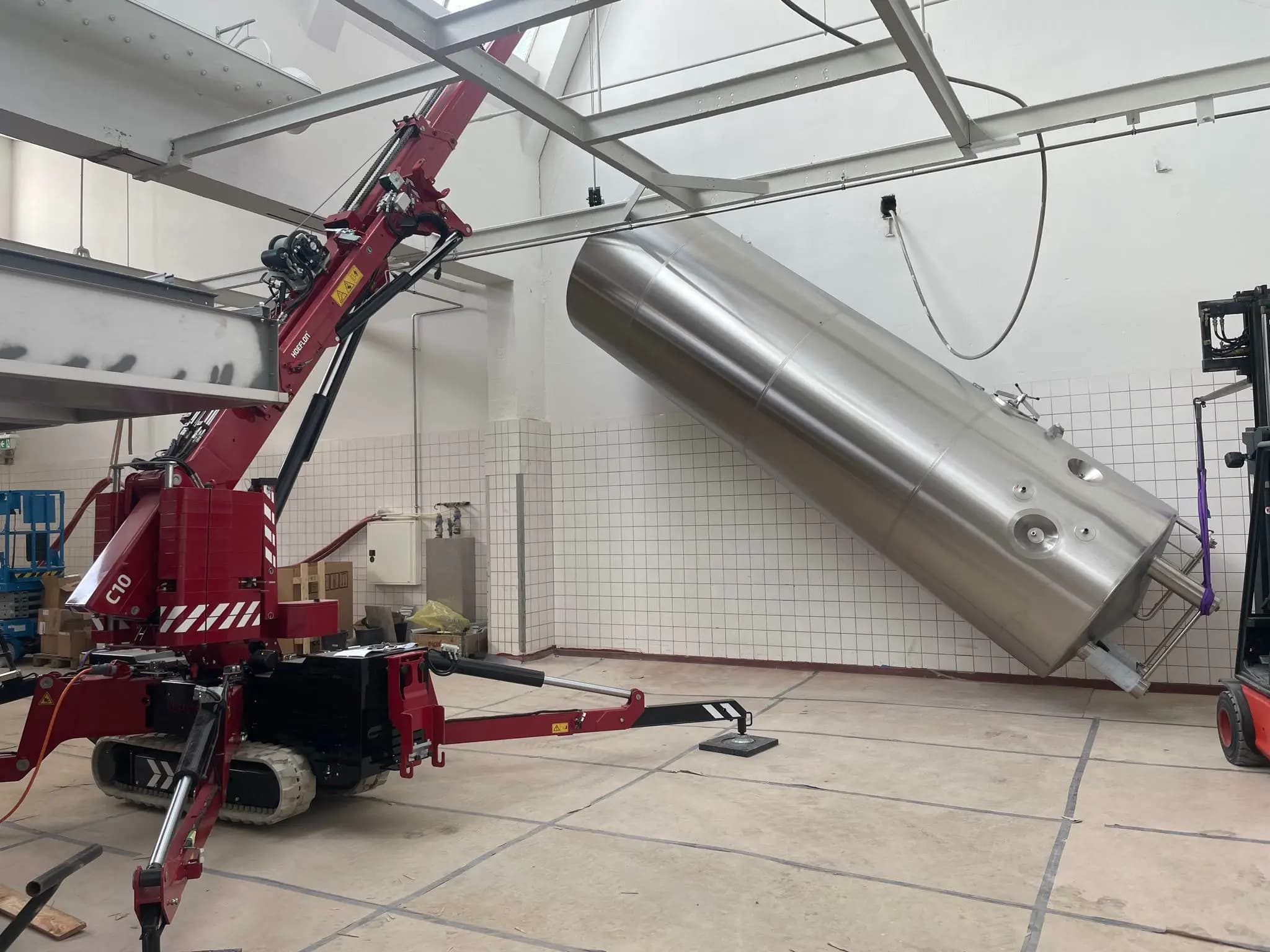 Hoeflon C10 levantando un gran cilindro en una nave industrial.