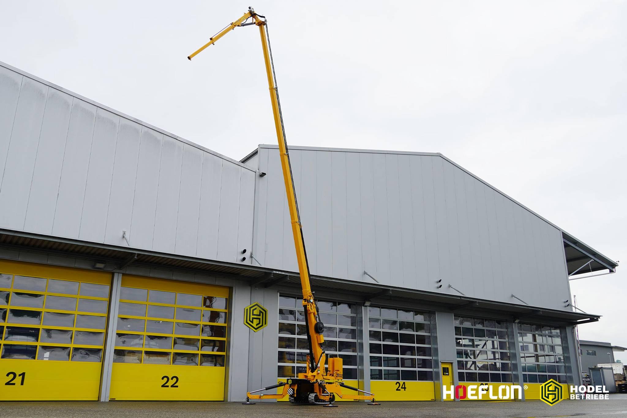 Grúa oruga Hoeflon C10e con brazo elevado para un edificio.