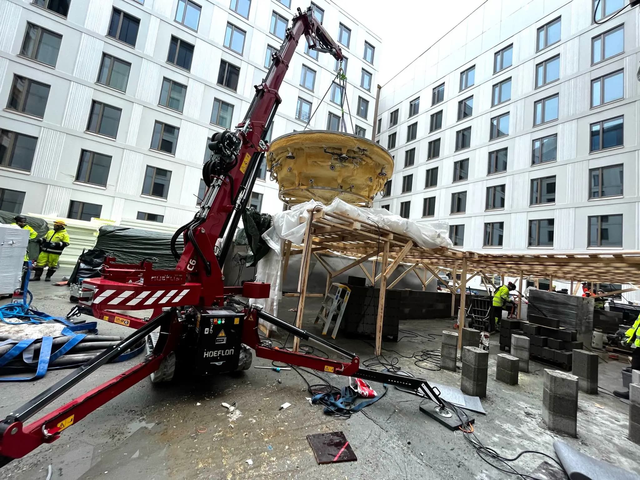 Grúa Hoeflon levantando objeto en la obra.